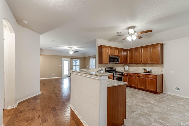 kitchen with light stone counters, kitchen peninsula, ceiling fan, stainless steel appliances, and decorative backsplash