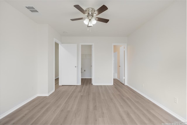 unfurnished bedroom featuring ceiling fan, a walk in closet, light wood-type flooring, and a closet