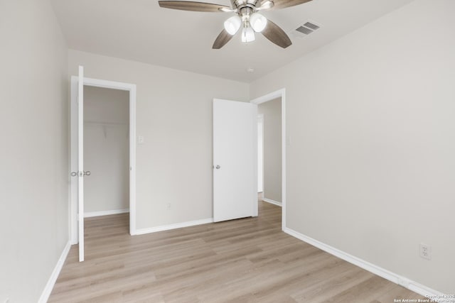 unfurnished bedroom with ceiling fan, a walk in closet, light wood-type flooring, and a closet