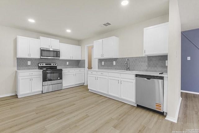 kitchen with sink, light wood-type flooring, white cabinets, and appliances with stainless steel finishes