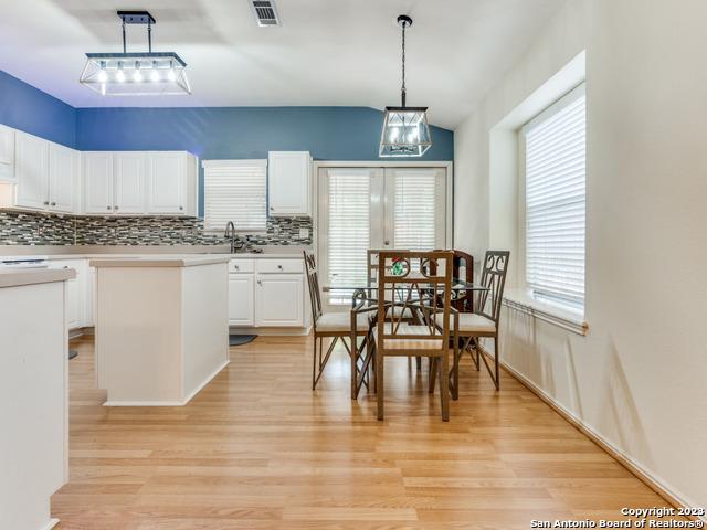 kitchen with pendant lighting, white cabinetry, lofted ceiling, backsplash, and light hardwood / wood-style flooring