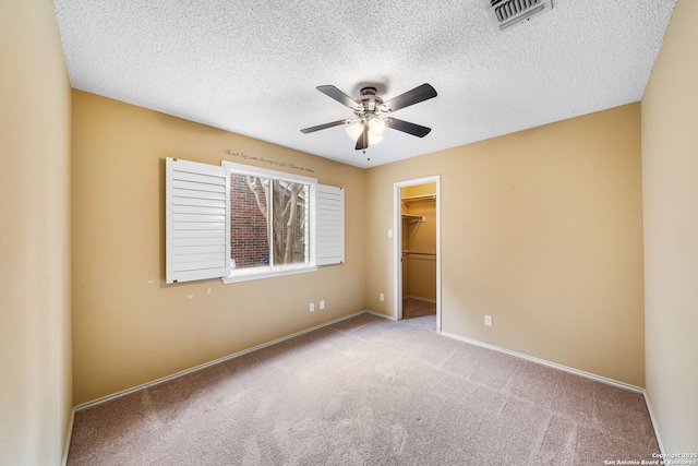 unfurnished bedroom with light colored carpet, a spacious closet, a closet, and a textured ceiling