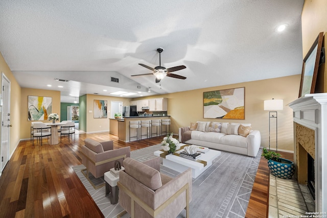 living room featuring vaulted ceiling, wood-type flooring, ceiling fan, and a textured ceiling