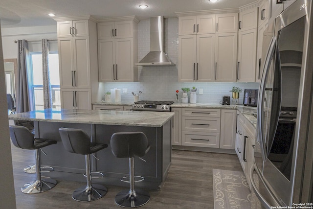 kitchen featuring a kitchen island, stainless steel refrigerator, white cabinetry, range, and wall chimney range hood