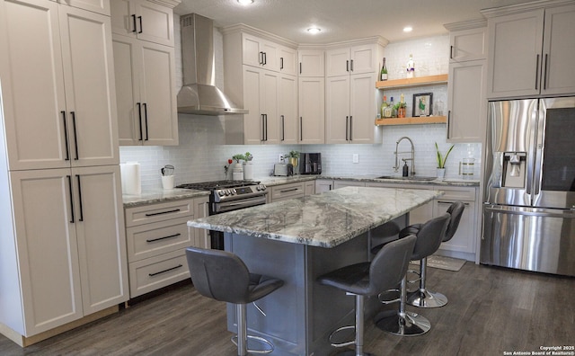 kitchen featuring sink, appliances with stainless steel finishes, a kitchen bar, a kitchen island, and wall chimney exhaust hood