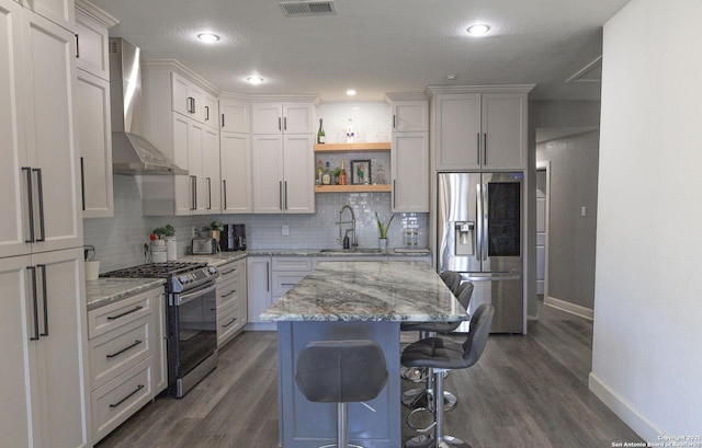 kitchen featuring sink, white cabinetry, appliances with stainless steel finishes, a kitchen island, and wall chimney range hood