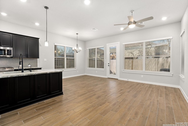 kitchen featuring hanging light fixtures, light wood-type flooring, light stone countertops, ceiling fan with notable chandelier, and backsplash