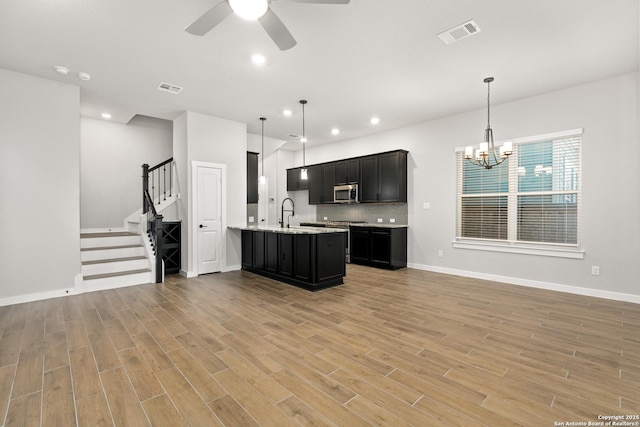 kitchen featuring appliances with stainless steel finishes, ceiling fan with notable chandelier, backsplash, hanging light fixtures, and light hardwood / wood-style floors