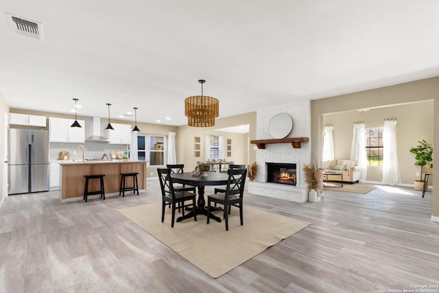 dining space with an inviting chandelier, a brick fireplace, and light wood-type flooring