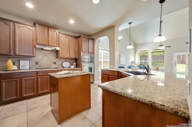 kitchen with sink, hanging light fixtures, stainless steel appliances, light stone countertops, and a center island with sink