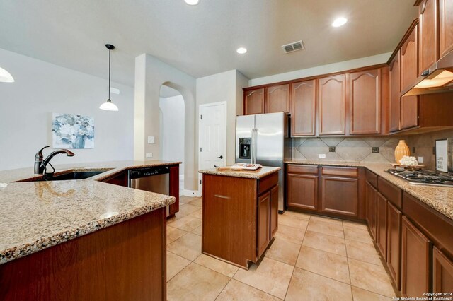 kitchen featuring sink, tasteful backsplash, decorative light fixtures, a center island, and light stone countertops