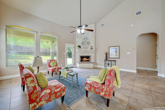 tiled living room with ceiling fan, high vaulted ceiling, and a brick fireplace