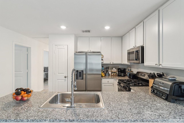 kitchen with stainless steel appliances, white cabinetry, sink, and light stone counters