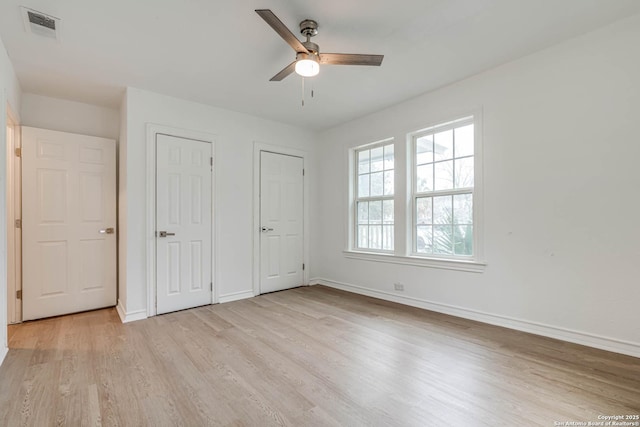 unfurnished bedroom featuring ceiling fan, light hardwood / wood-style floors, and two closets