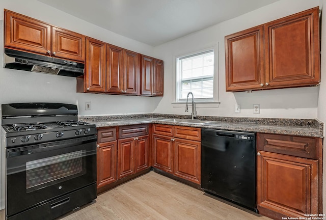 kitchen with sink, black appliances, dark stone counters, and light wood-type flooring