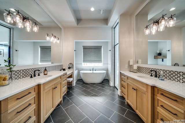 bathroom with tile patterned floors, tasteful backsplash, vanity, a tray ceiling, and a bath