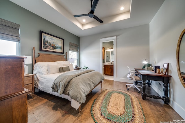 bedroom with a raised ceiling, wood-type flooring, ensuite bathroom, and ceiling fan