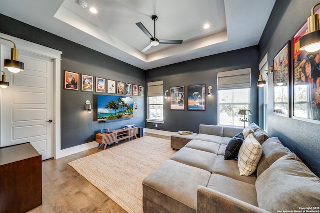 home theater with ceiling fan, a raised ceiling, and hardwood / wood-style floors