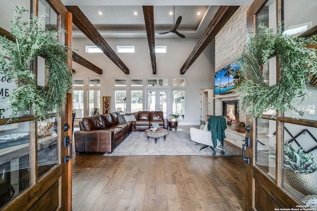 living room featuring a stone fireplace, high vaulted ceiling, dark hardwood / wood-style flooring, beam ceiling, and french doors