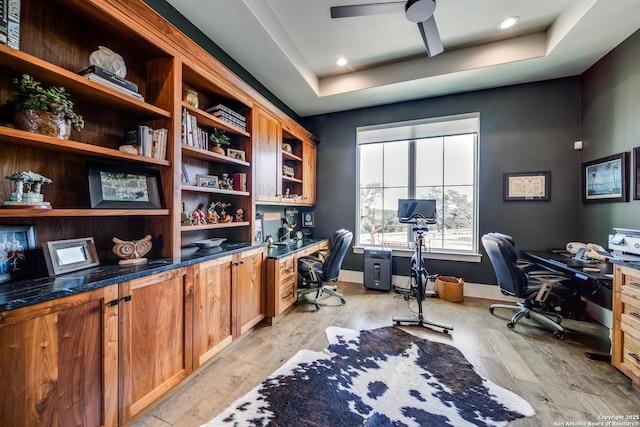 office featuring ceiling fan, a tray ceiling, and light wood-type flooring