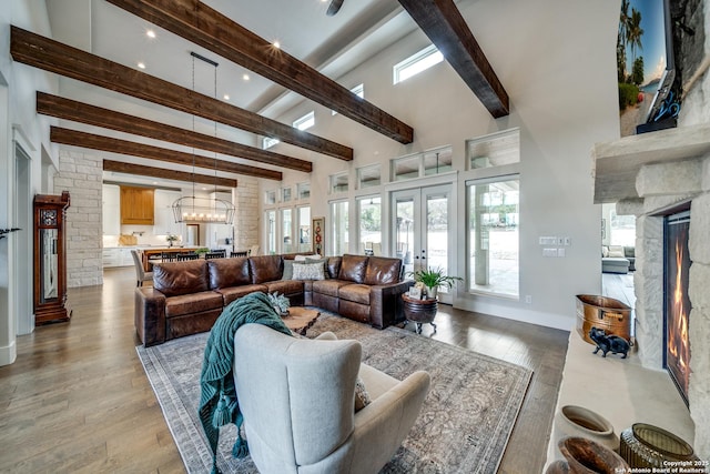 living room featuring beam ceiling, a towering ceiling, a high end fireplace, wood-type flooring, and french doors