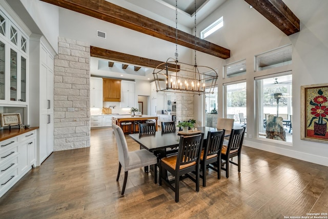 dining area with beamed ceiling, a towering ceiling, a notable chandelier, and dark hardwood / wood-style flooring