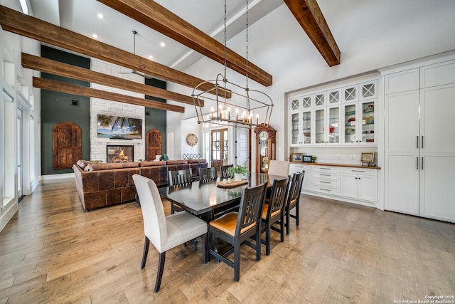 dining space featuring beamed ceiling, high vaulted ceiling, light wood-type flooring, and a fireplace