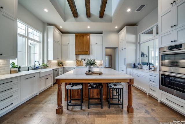 kitchen featuring a kitchen bar, sink, white cabinetry, a kitchen island, and stainless steel appliances