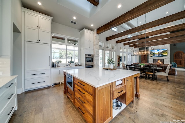 kitchen with a fireplace, white cabinets, light stone countertops, light wood-type flooring, and a spacious island