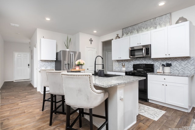 kitchen with sink, a breakfast bar area, a center island with sink, stainless steel appliances, and white cabinets