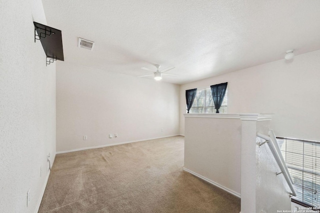 empty room featuring ceiling fan, light colored carpet, and a textured ceiling