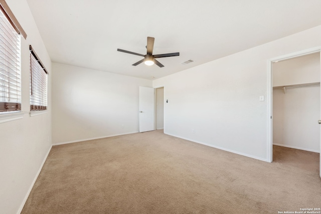 unfurnished bedroom with ceiling fan, a walk in closet, a closet, and light carpet