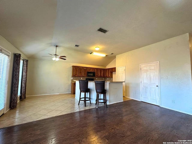 kitchen with vaulted ceiling, a breakfast bar, backsplash, ceiling fan, and light hardwood / wood-style flooring