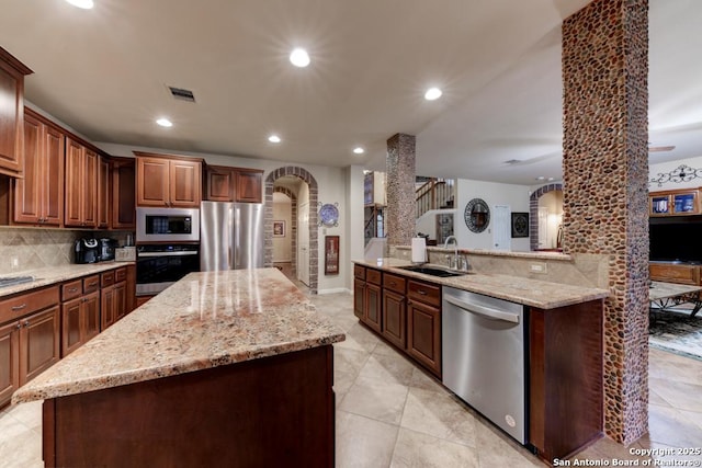 kitchen with sink, appliances with stainless steel finishes, a kitchen island, decorative backsplash, and kitchen peninsula