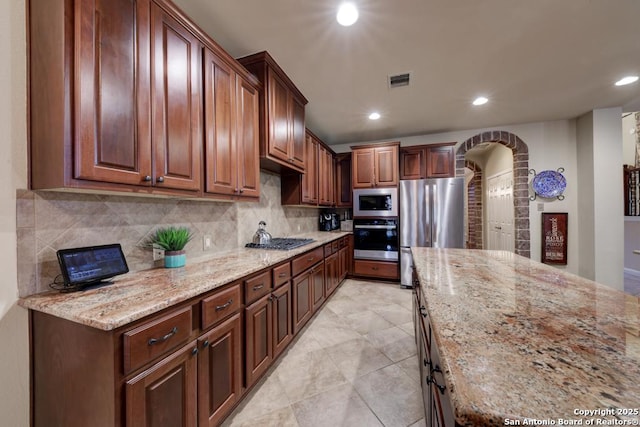 kitchen with light stone counters, stainless steel appliances, and backsplash