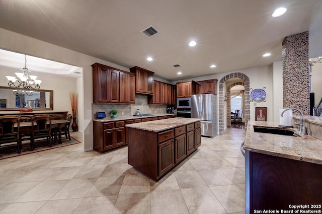 kitchen with stainless steel appliances, sink, light stone counters, and decorative light fixtures