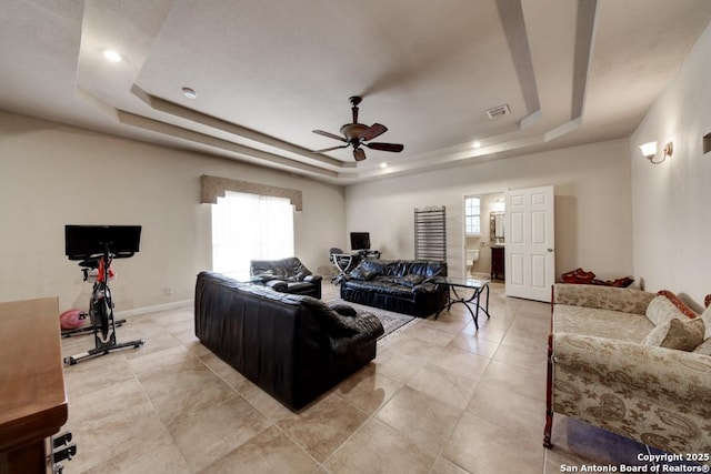 tiled living room with ceiling fan and a tray ceiling