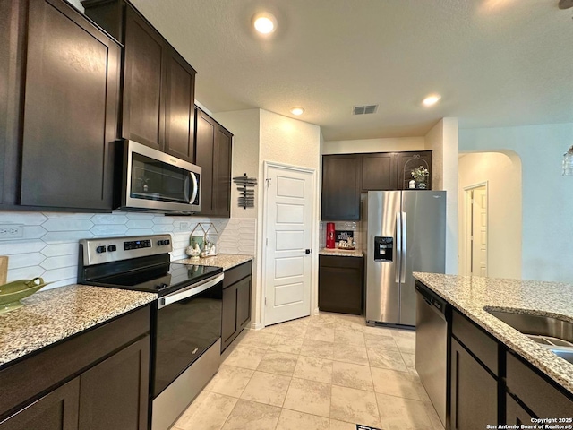 kitchen with dark brown cabinetry, tasteful backsplash, light stone countertops, and appliances with stainless steel finishes