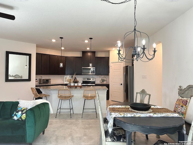 kitchen with pendant lighting, stainless steel appliances, a center island, dark brown cabinetry, and light stone countertops