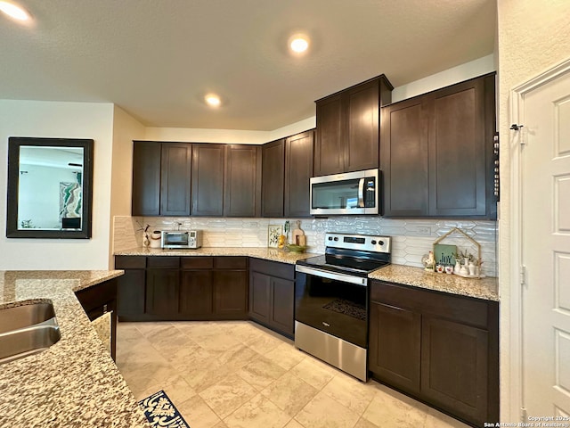 kitchen featuring dark brown cabinetry, light stone countertops, decorative backsplash, and stainless steel appliances