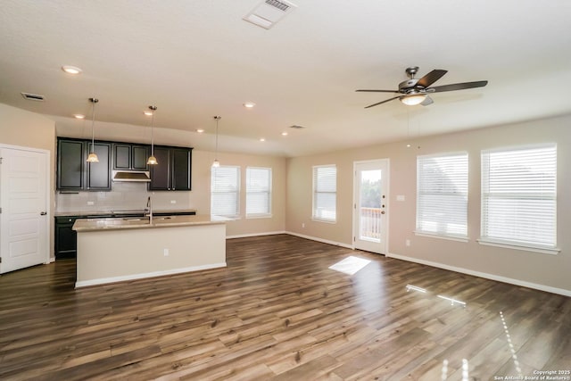 kitchen with a kitchen island with sink, pendant lighting, dark hardwood / wood-style flooring, and decorative backsplash