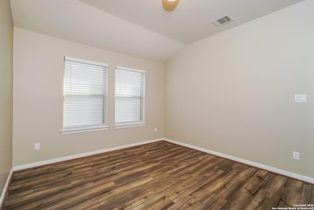 spare room featuring dark wood-type flooring and vaulted ceiling