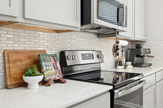 kitchen featuring light stone countertops, decorative backsplash, stainless steel appliances, and white cabinets