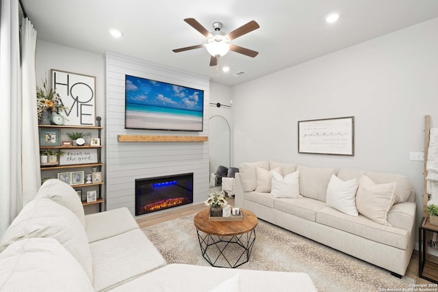 living room with a large fireplace, hardwood / wood-style floors, and ceiling fan