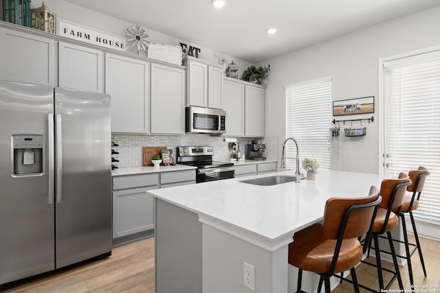 kitchen featuring sink, gray cabinetry, a kitchen island with sink, light stone counters, and stainless steel appliances