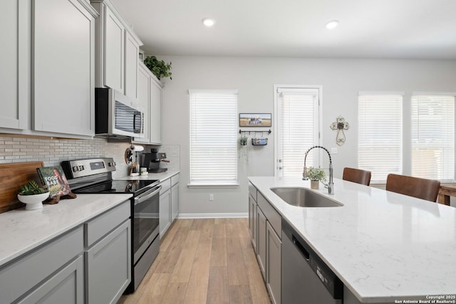 kitchen featuring sink, light stone counters, tasteful backsplash, light wood-type flooring, and appliances with stainless steel finishes