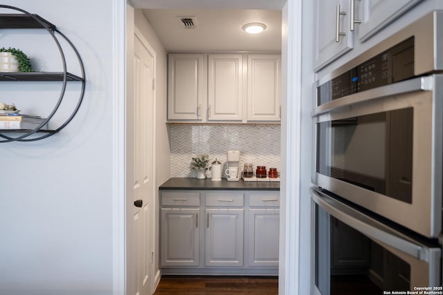 kitchen featuring double oven, backsplash, dark hardwood / wood-style floors, and white cabinets