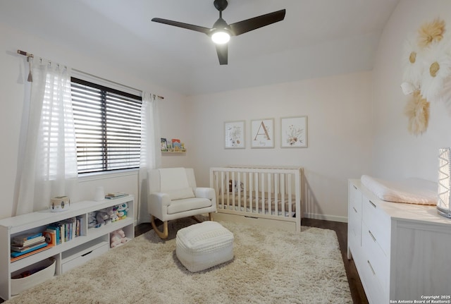 bedroom featuring a crib, dark hardwood / wood-style floors, and ceiling fan