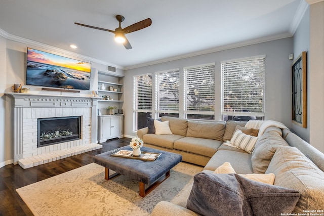 living room featuring a brick fireplace, dark wood-type flooring, ornamental molding, and a healthy amount of sunlight