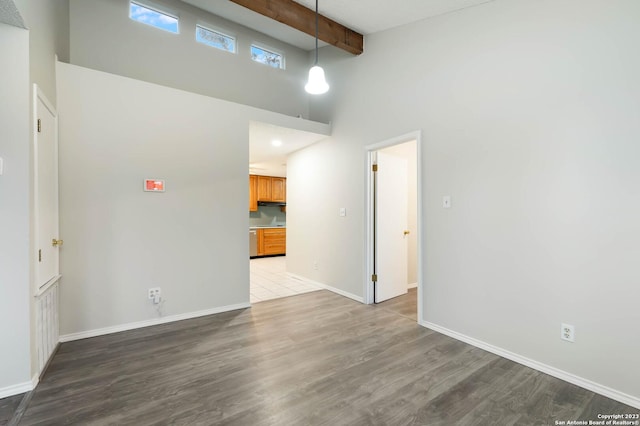 spare room featuring a towering ceiling, wood-type flooring, and beam ceiling